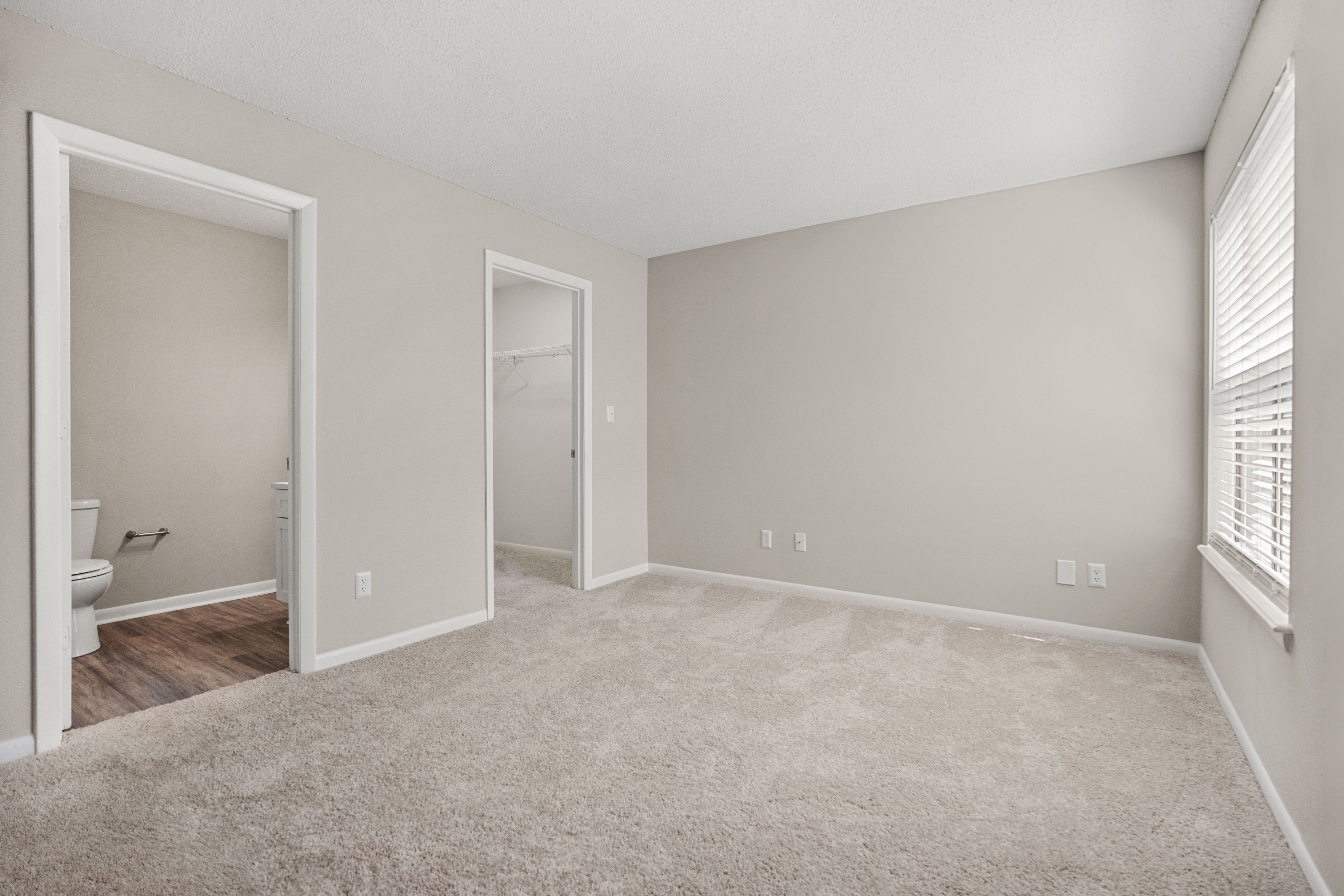 A spacious room with a carpeted floor and a window with blinds.