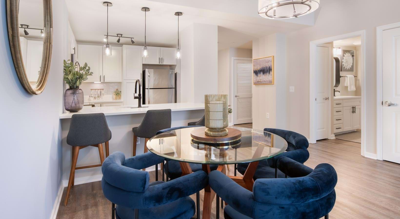 An interior view of a kitchen and dining area with a dining table and chairs, as well as a bathroom with a vanity countertop and a large mirror at Pearson Square apartments in Falls Church, VA