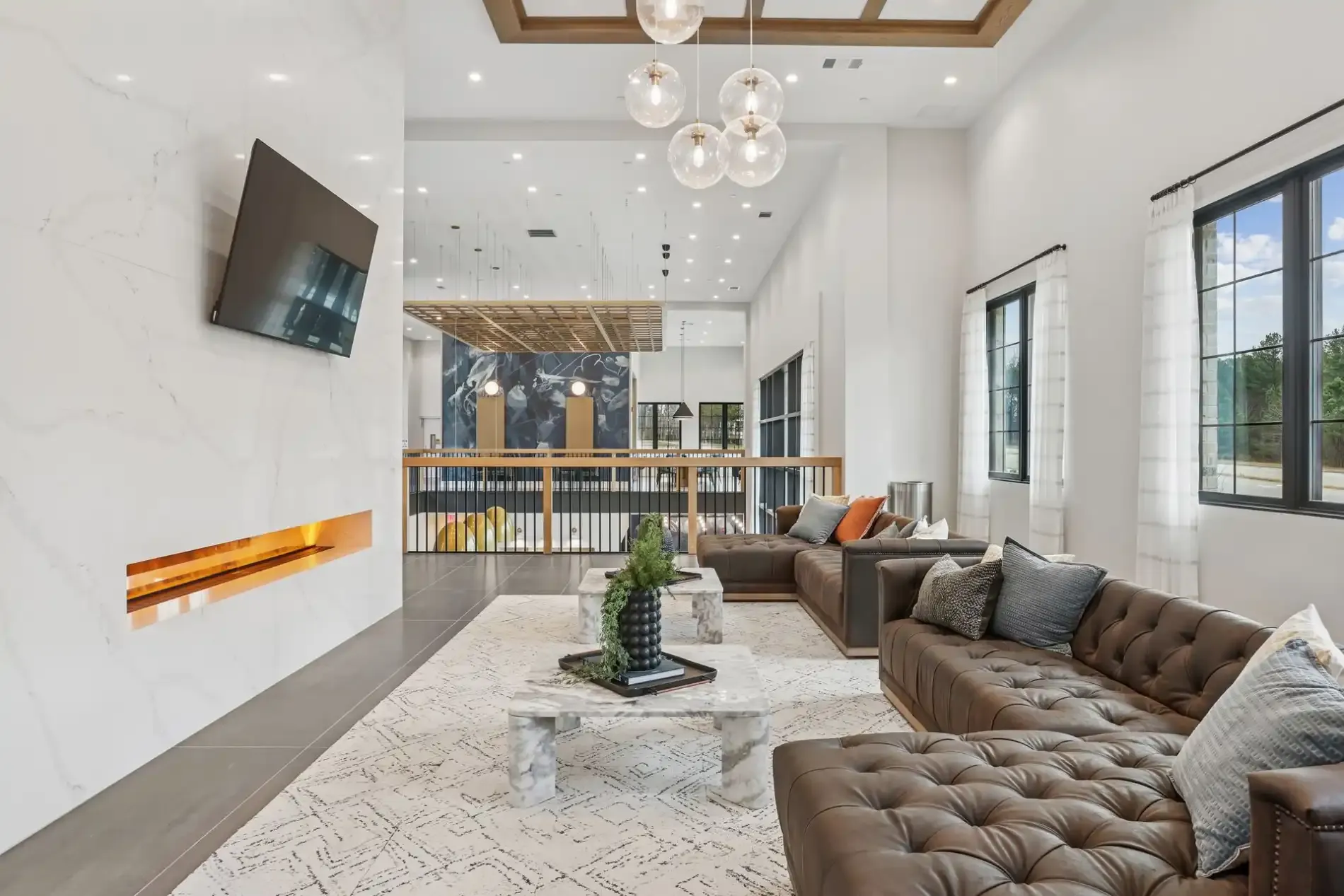 Modern living room with a brown tufted sofa, white stone fireplace, tv, and gold-accented lighting.