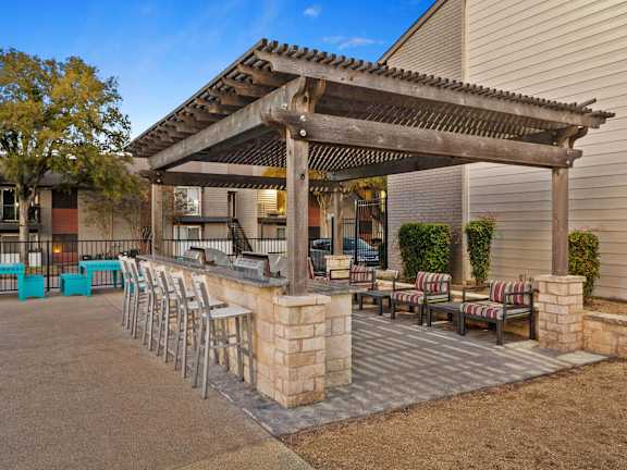 A patio with a pergola and chairs is set up outside a house.