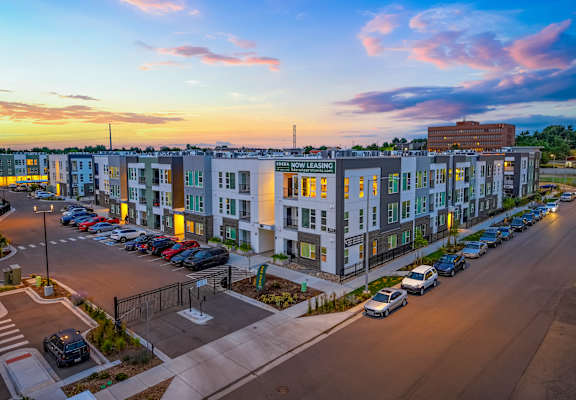 A sunset view of a parking lot in front of a multi-story apartment complex.