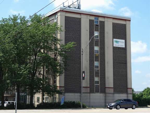 A grey car is parked in front of a building with a sign that reads "The Pines".