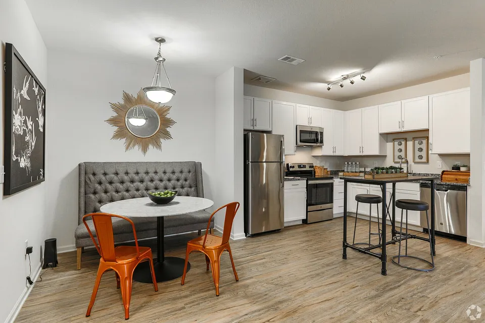 Modern kitchen featuring stainless steel appliances, white cabinetry, and a cozy dining area with stylish orange chairs.