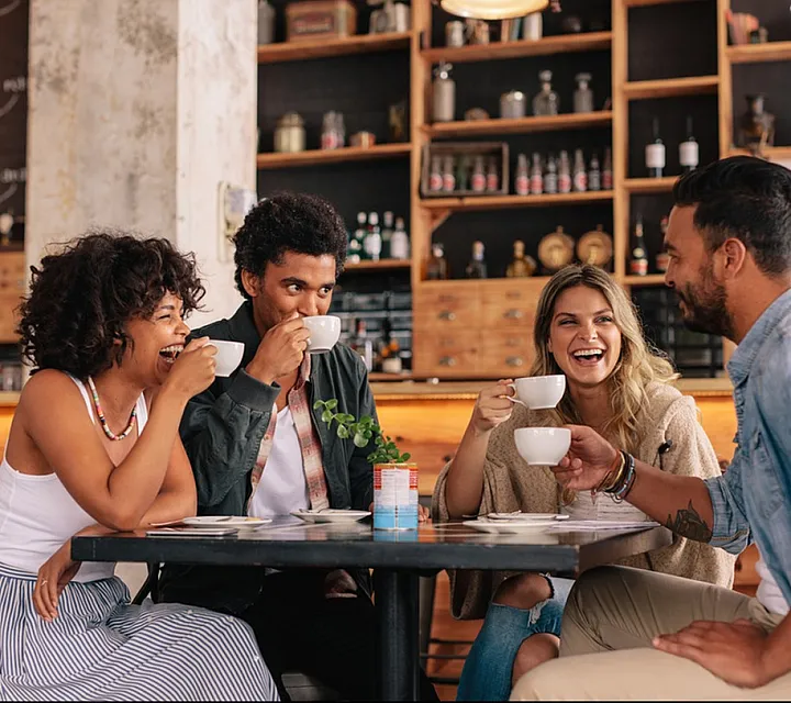 Group of friends enjoying coffee and laughter in a cozy café setting with rustic decor.