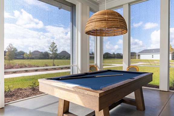 Pool table on a screened-in porch with a hanging lamp.
