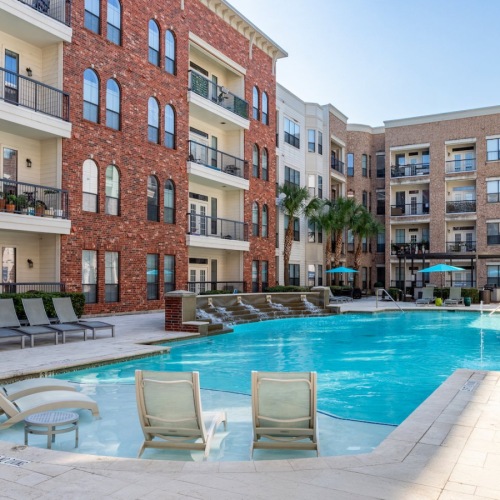 Tanglewood, Houston, TX, Apartments - Forum on San Felipe - Resort-Style Pool with Rippling Fountain Wall with Multiple Lounge Seats, Tanning Ledge, and the Apartment View.