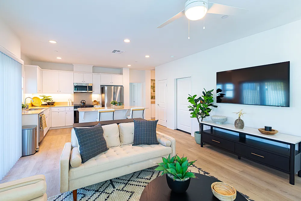 Bright, modern living room with open-concept kitchen boasting sleek white cabinetry, stainless steel appliances, and stylish decor.