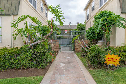 a walkway between two apartment buildings with a fence and palm trees