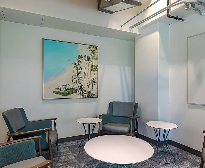 Cozy seating area with modern chairs and chic round tables, featuring a stunning beach artwork on the wall, creating a relaxing ambiance.