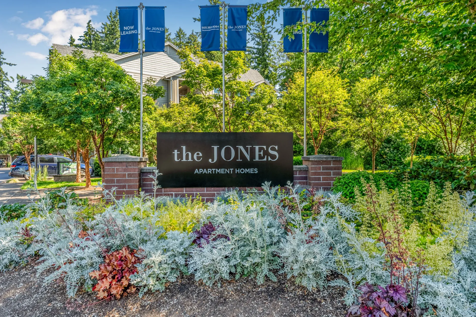 Exterior sign for the JONES Apartment Homes with surrounding landscaping and blue leasing banners.