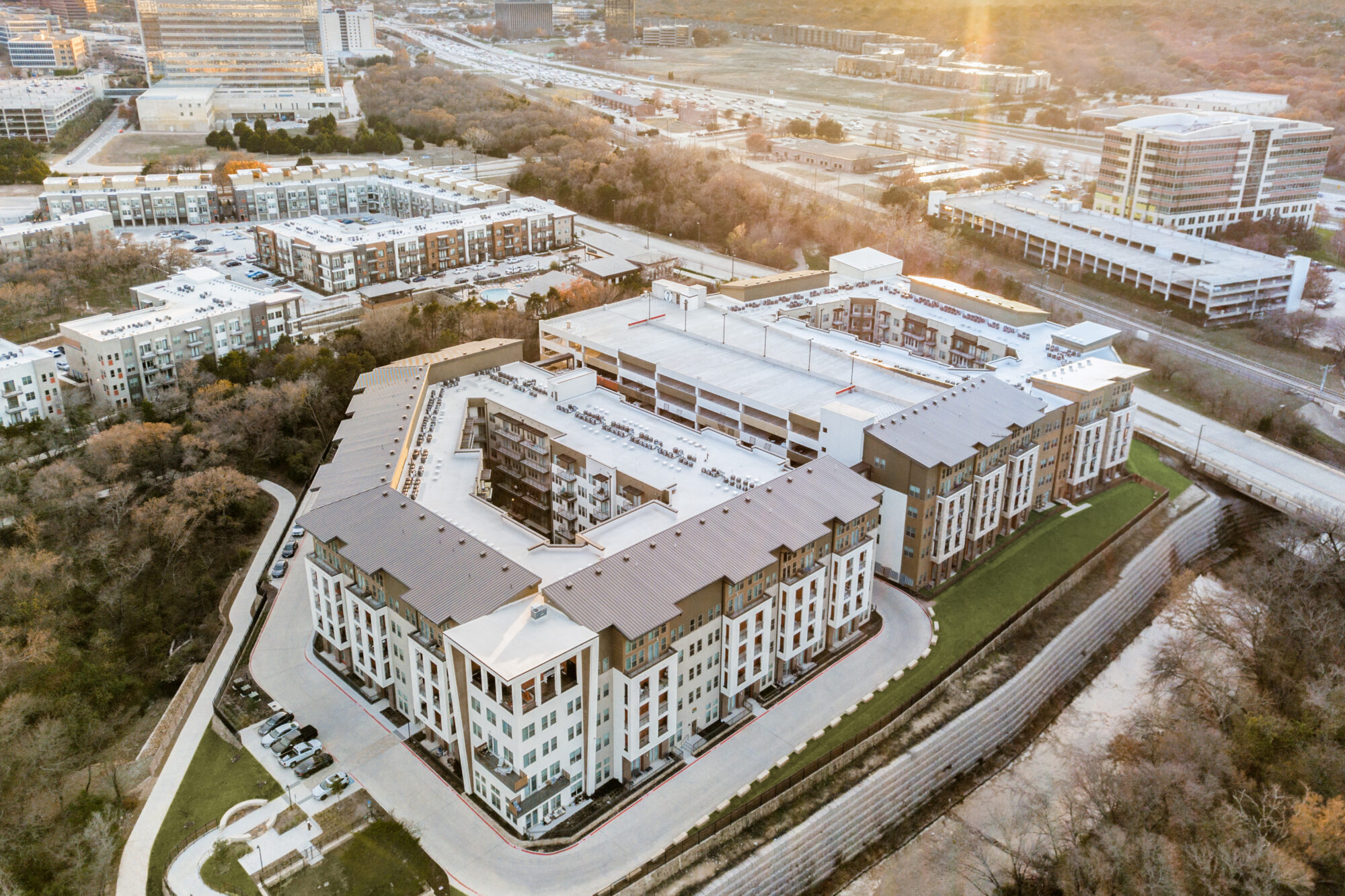 aerial view of the community with other buildings in the background and nature trail in the foreground