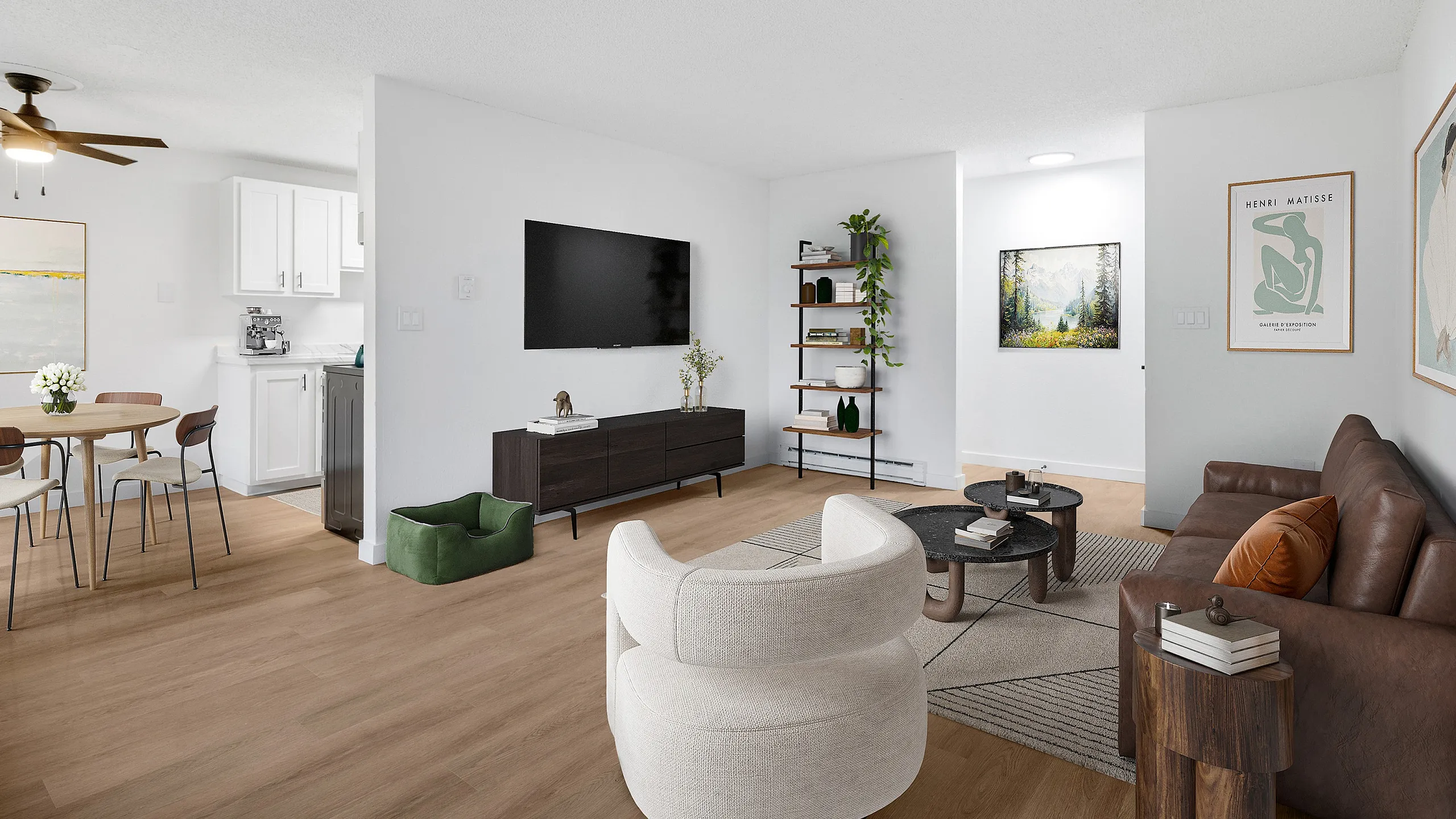 Bright and inviting open-concept living room with modern furnishings, featuring a cozy brown leather couch, chic round tables, and a stylish dining area adjacent to a sleek kitchen.