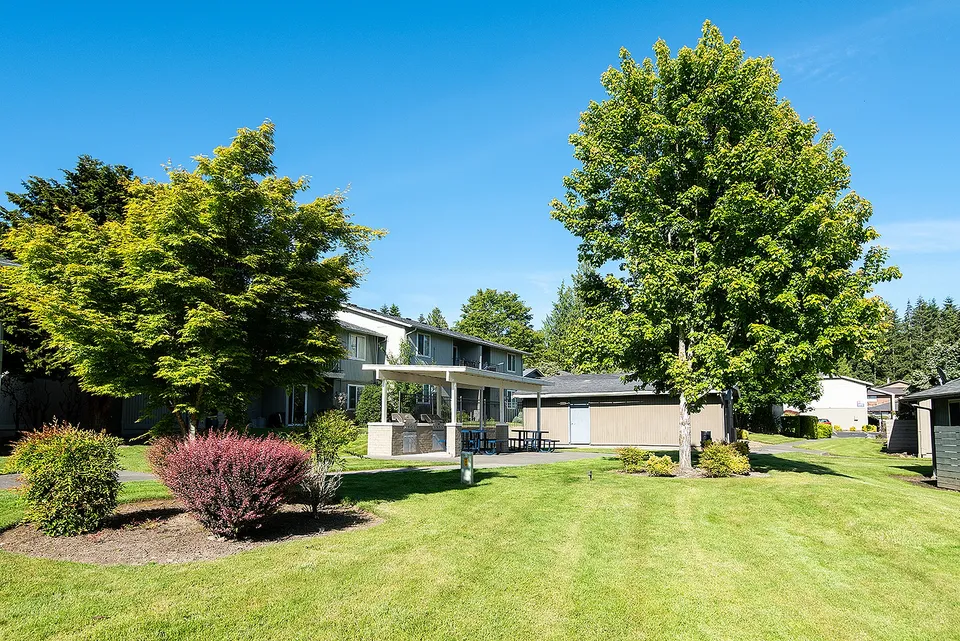Charming suburban apartment with lush green landscaping, vibrant trees, and a cozy outdoor seating area under blue skies.