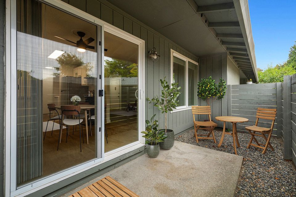 Charming patio with cozy seating and potted plants, viewed through sliding glass doors, perfect for indoor-outdoor living.