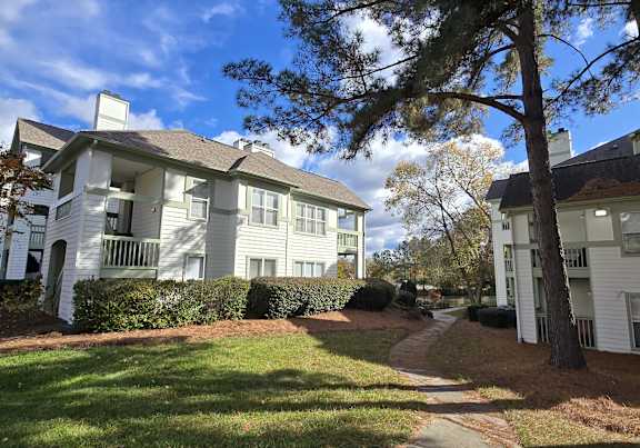 A white apartment building with a tree in front.