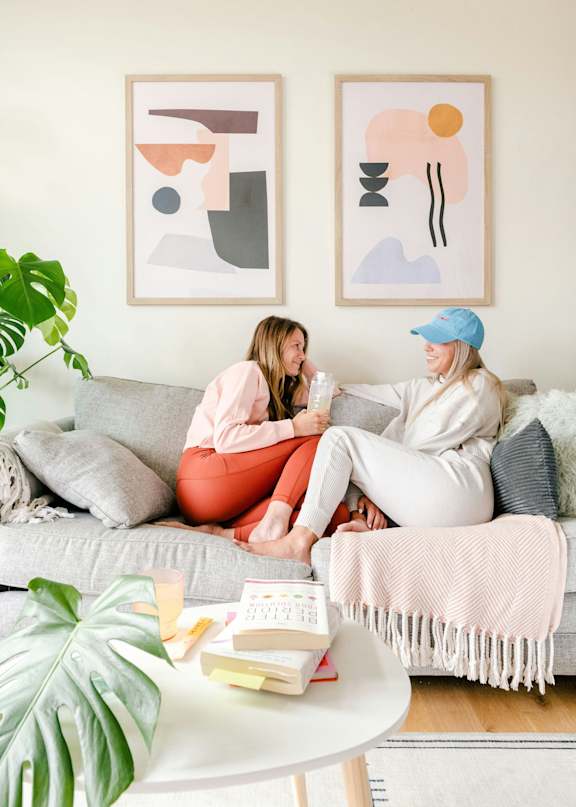 Two women sitting on a couch with a book and a plant in front of them.