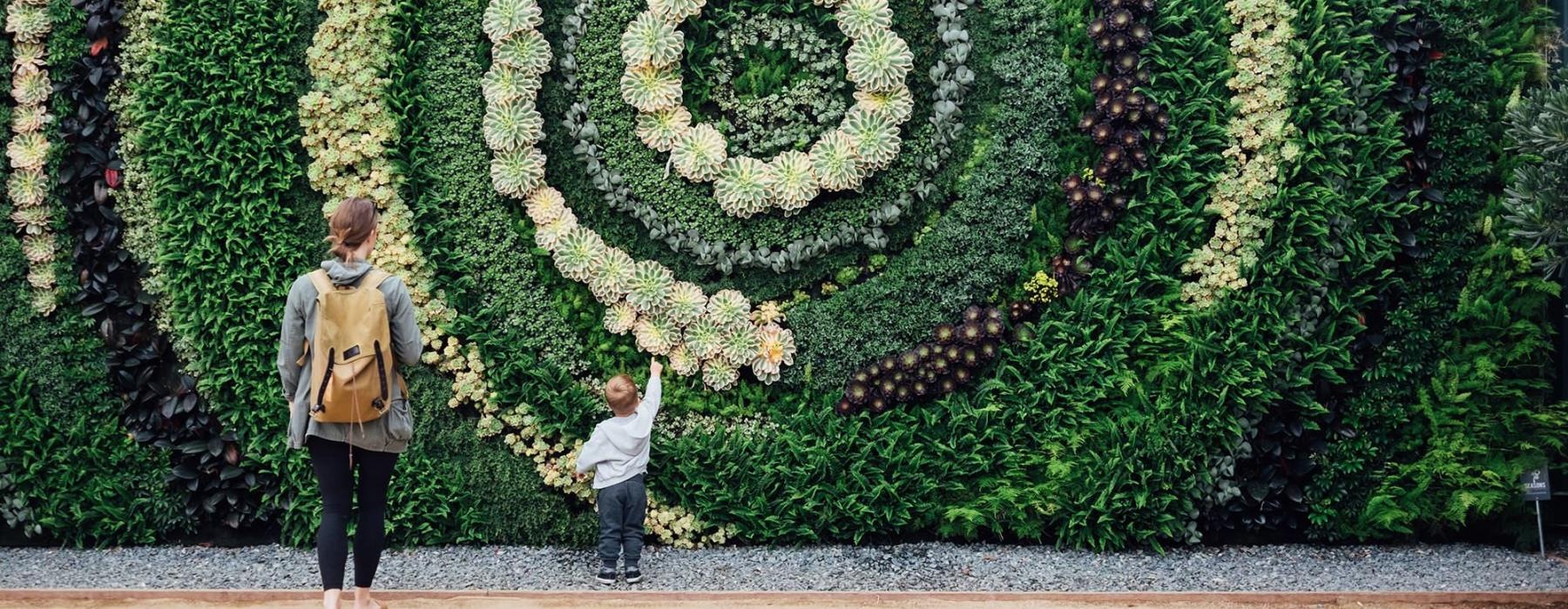 mother and child standing in front of a mural made of plants