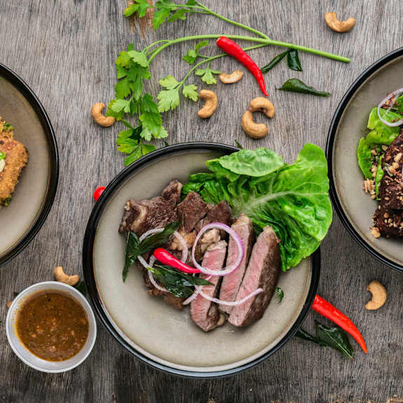 A plate of sliced beef with onions and herbs is on a wooden table.