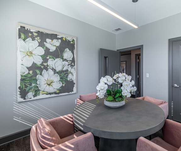A grey table with a vase of flowers on it and two chairs with pink cushions.
