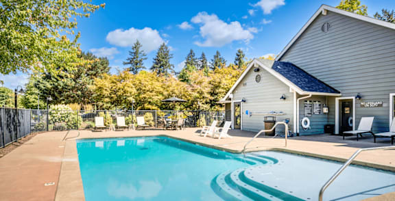 A pool with chairs and umbrellas in front of a house.