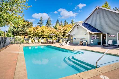 A swimming pool in front of a house with trees in the background.