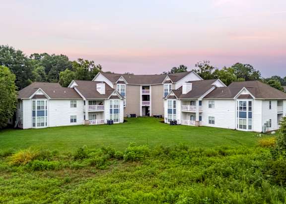 A large white building with multiple windows and balconies is surrounded by greenery.