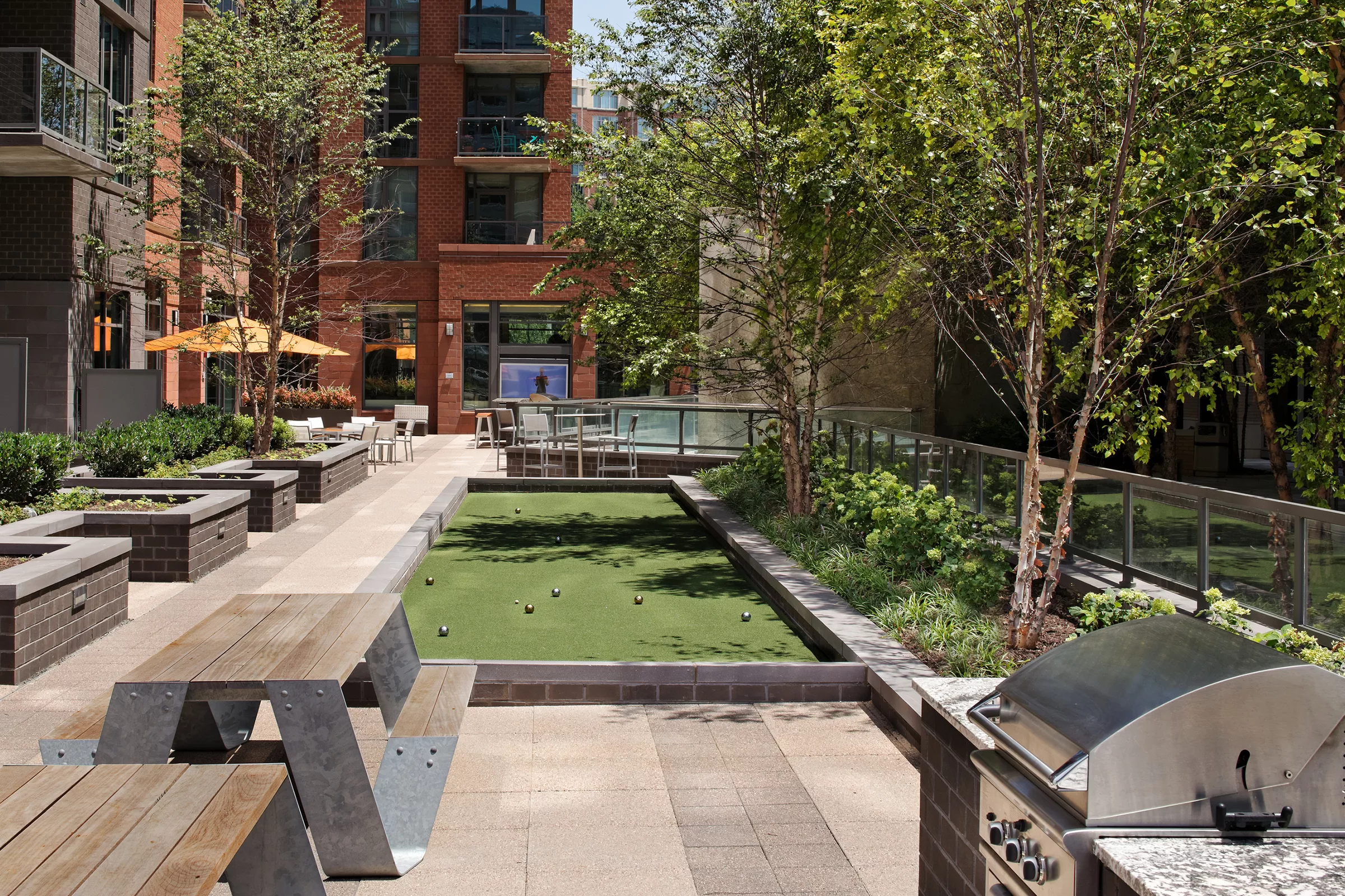 outdoor courtyard at Parc Riverside apartments in DC with bocce court, grill and various seating areas lined with trees