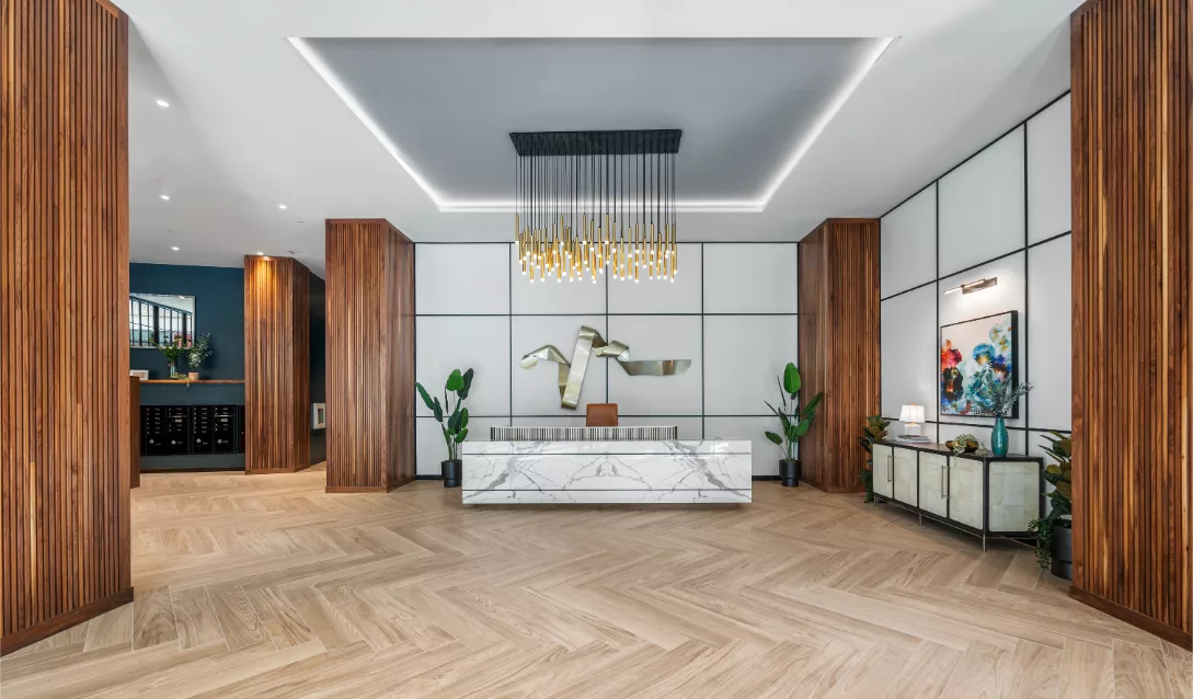Lobby with marble front desk, modern hanging lights, large wooden columns, and chevron wood flooring.