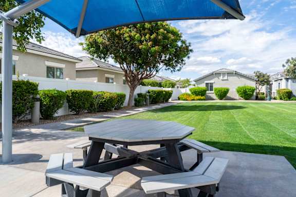 A picnic table with a blue umbrella is set up on a concrete slab at Vistoria At Country Place Apartments, Tolleson