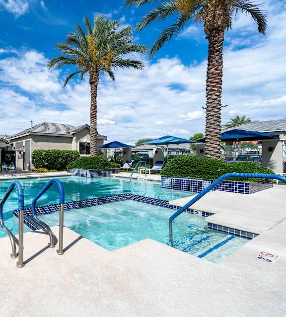 A swimming pool surrounded by palm trees and residential houses at Vistoria At Country Place Apartments, Tolleson, AZ, 85353