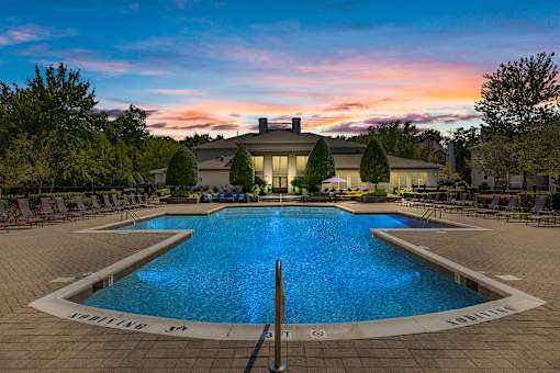 A large swimming pool in front of a house with a sunset in the background.