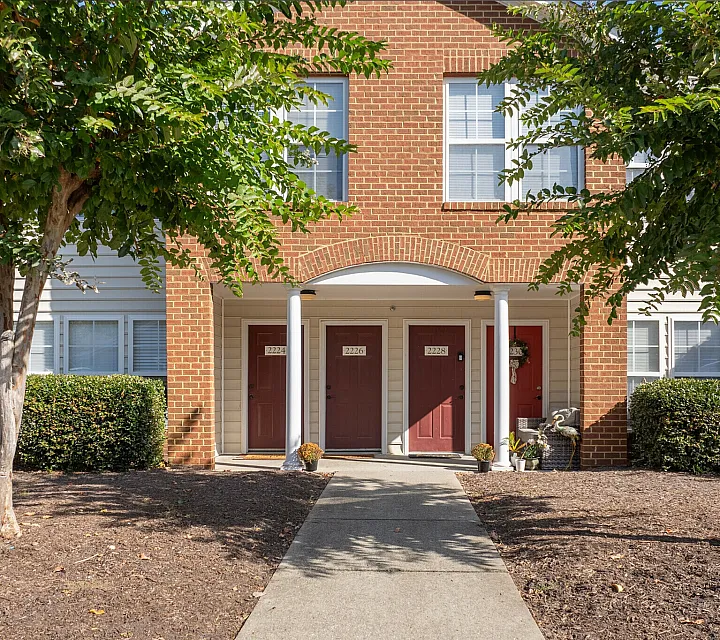 Welcoming brick facade with red doors surrounded by greenery and white columns.