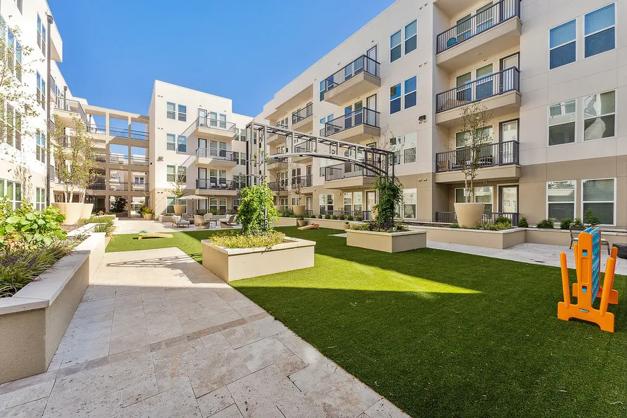sunny outdoor courtyard next to a four-story apartment building with private balconies