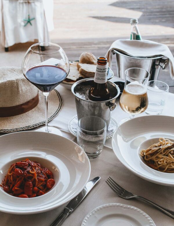 Table with elegant pasta dishes, glasses of wine, and bowls of bread.