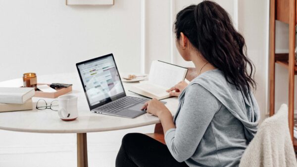 Person working at table with laptop computer, book, and cup of tea.