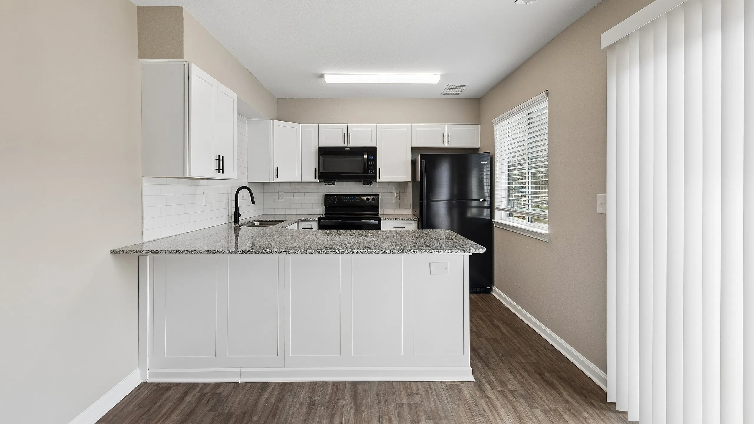Modern kitchen with elegant granite countertops, sleek black appliances, and abundant natural light.