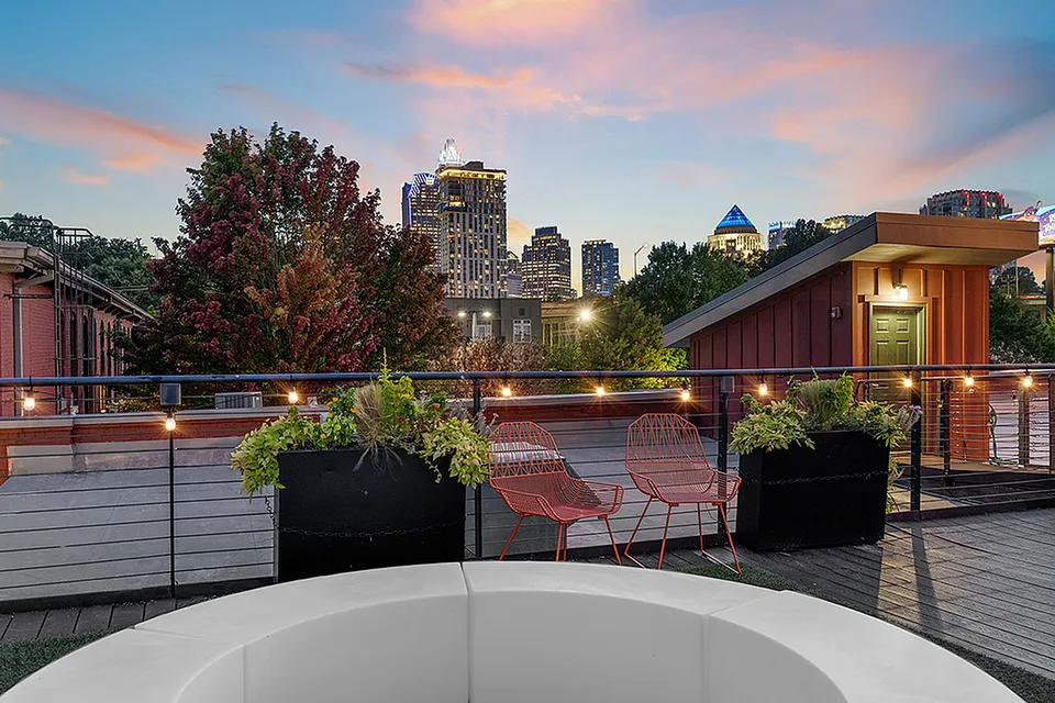 Charming rooftop patio with vibrant city skyline views, featuring cozy seating and lush greenery under a picturesque sunset at Alpha Mill Apartments in Uptown Charlotte NC