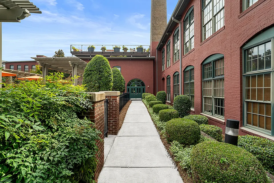 Charming apartment entrance with red brick exterior, lush greenery, and elegant windows at Alpha Mill Apartments in Charlotte NC