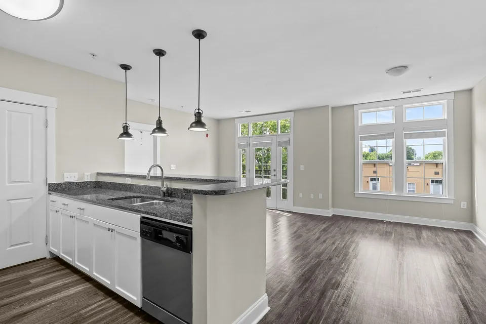 Bright and modern open-concept kitchen and living area featuring sleek granite countertops, elegant pendant lighting, and large windows for abundant natural light at Alpha Mill Apartments in Uptown Charlotte NC