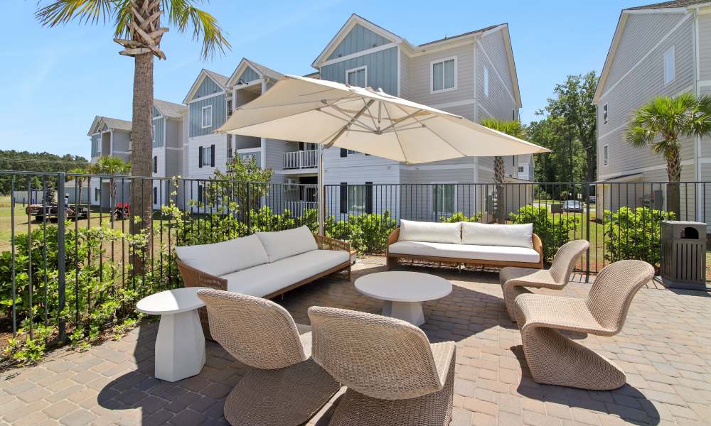 Outdoor lounge area with modern seating and umbrella near apartment buildings and greenery at Everett at Port Wentworth in Port Wentworth, Georgia