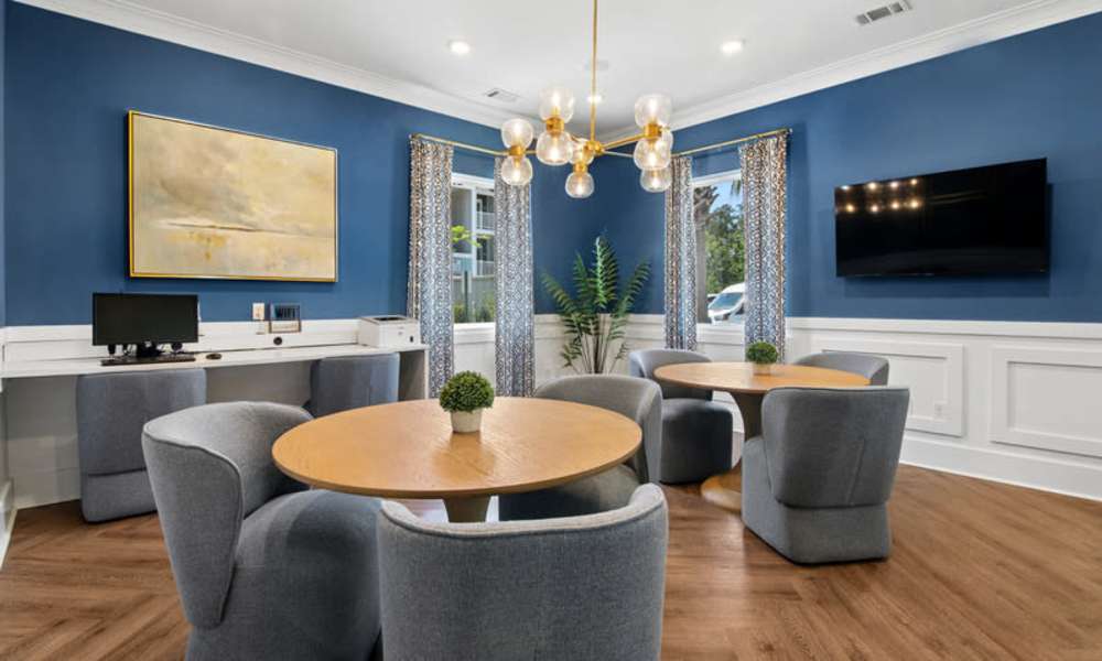 Bright community room with wood-style flooring, modern lighting, and cozy seating around circular tables at Everett at Port Wentworth in Port Wentworth, Georgia