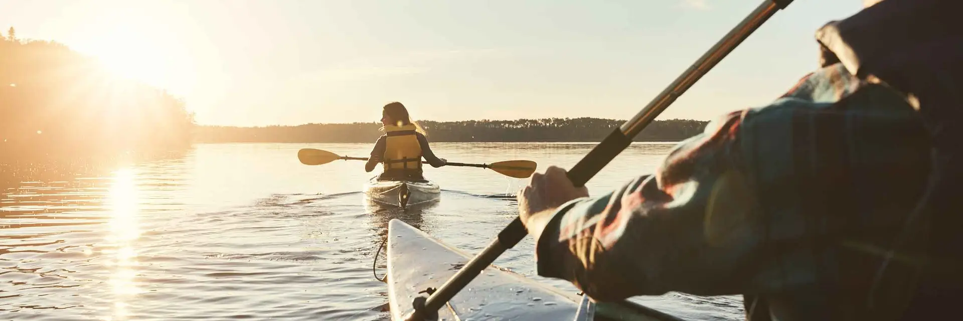 Two people kayaking at sunset on a calm lake.