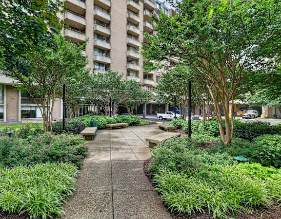 A concrete walkway leads through a landscaped area with a large building in the background.