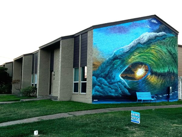 Colorful mural of a wave eye on the side of a building with a blue bench in front.