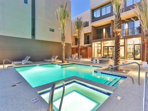 Apartments in Old Town Scottsdale, AZ - Dusk Scottsdale - 24-Hour Pool and Spa with Lounge Chairs, Apartment Building and Fitness Center in Background and Palm Trees.
