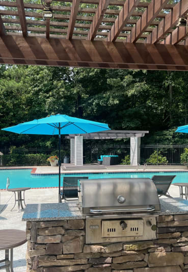 a pergola with a grill and umbrellas overlooking a swimming pool