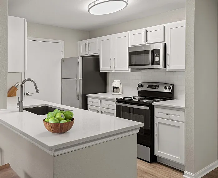Modern kitchen with sleek white cabinetry, stainless steel appliances, and a breakfast bar with wooden stools, accented by a bowl of fresh green apples.
