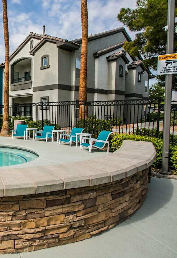 A pool surrounded by a stone wall with chairs and palm trees.