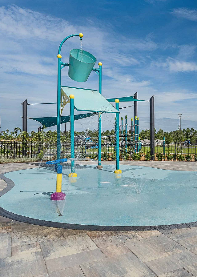Vibrant outdoor splash pad with playful water features and bright-colored structures set against a clear blue sky.