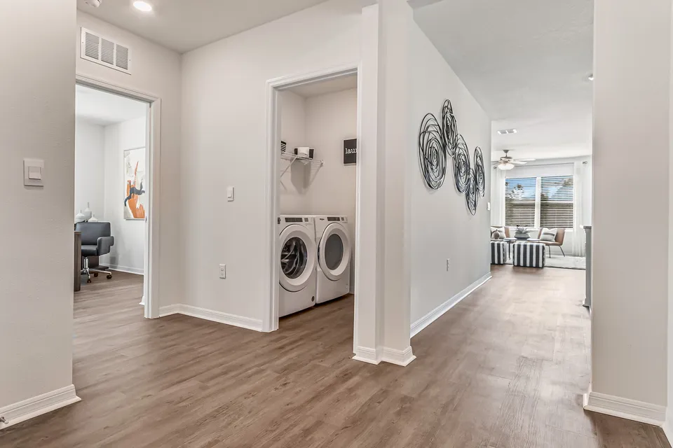 Modern hallway with elegant wood flooring, leading to a bright living room and state-of-the-art laundry area, accented with stylish wall art.